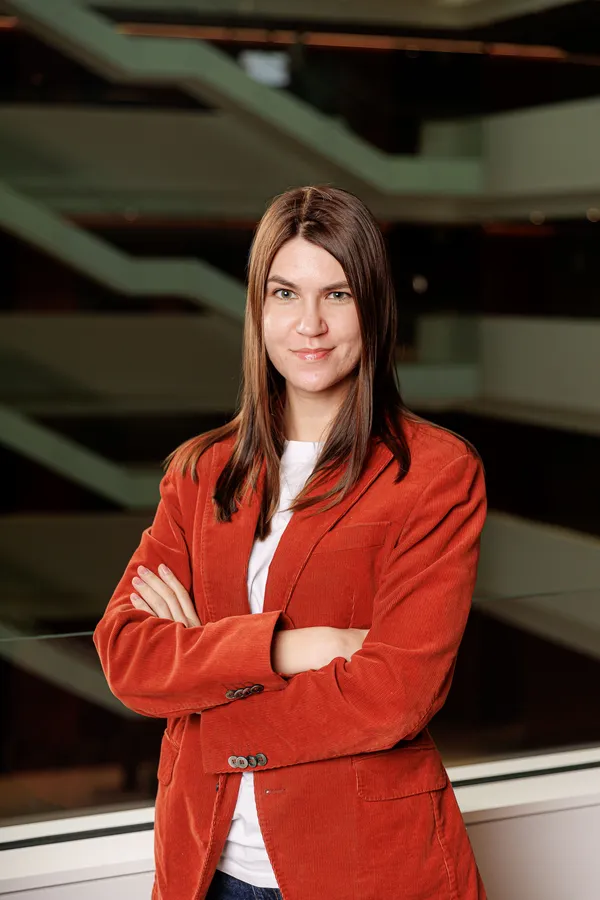 Woman with arms crossed in a rust-red blazer